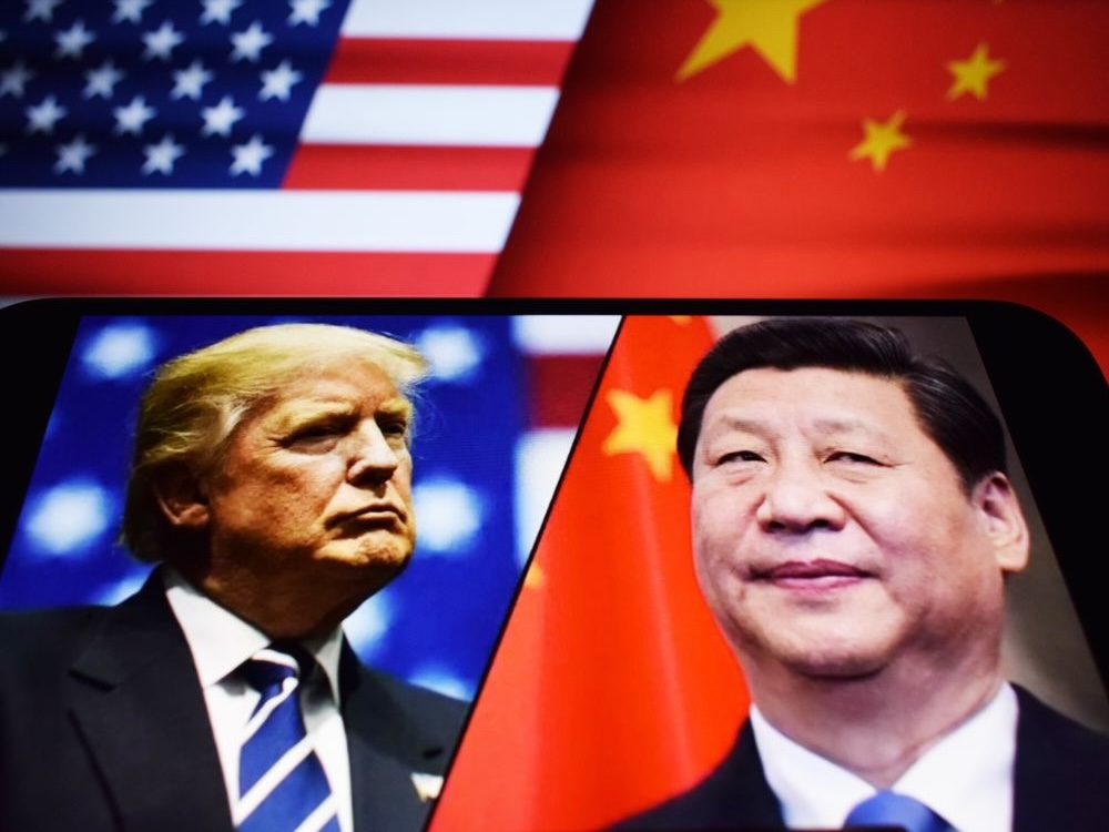 A cellphone shows images of Donald Trump and Xi Jinping and behind them portions of the U.S. and Chinese flags.