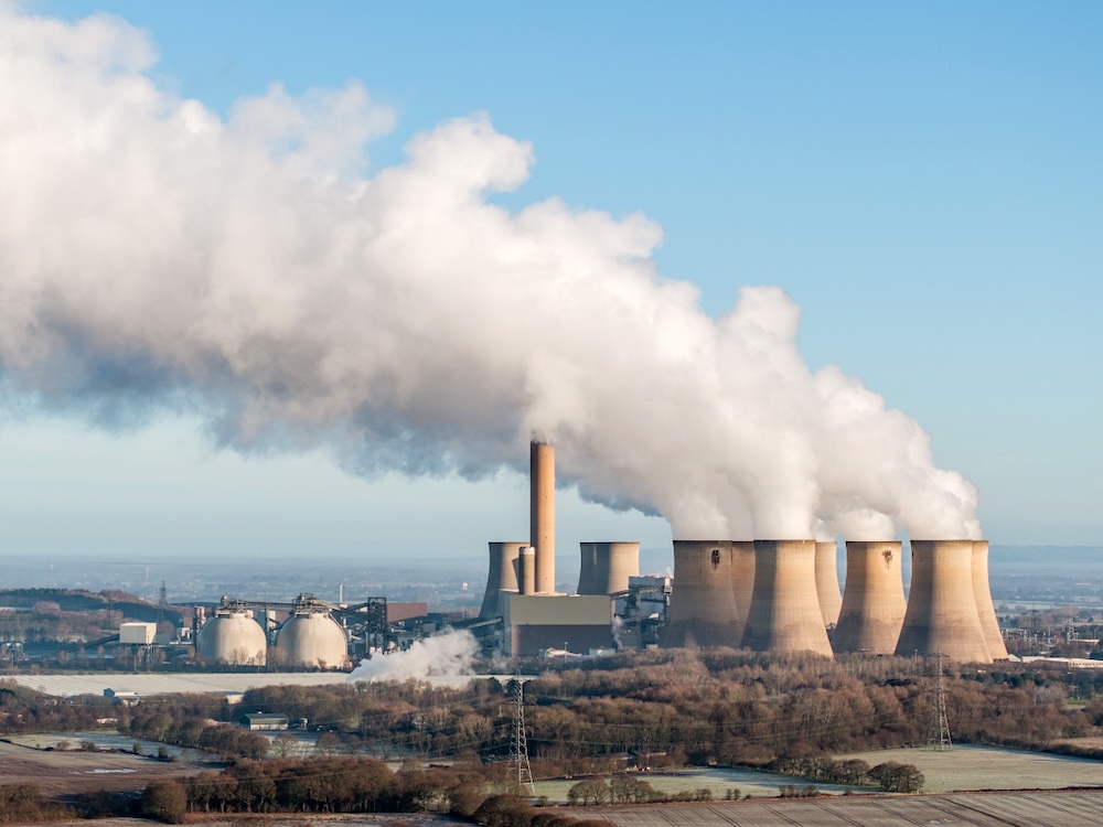 Steam rises from the massive stacks of a large power plant complex.