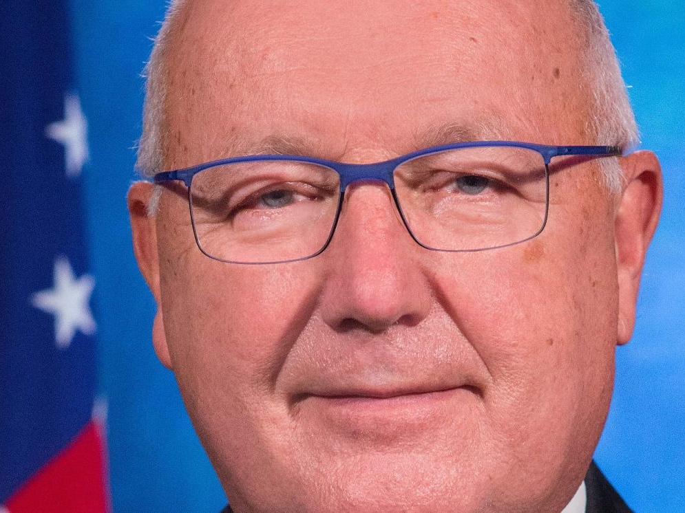 Close-up of the face of Pete Hoekstra, an older man with florid light skin tone and thinning white hair, wearing blue-framed glasses.
