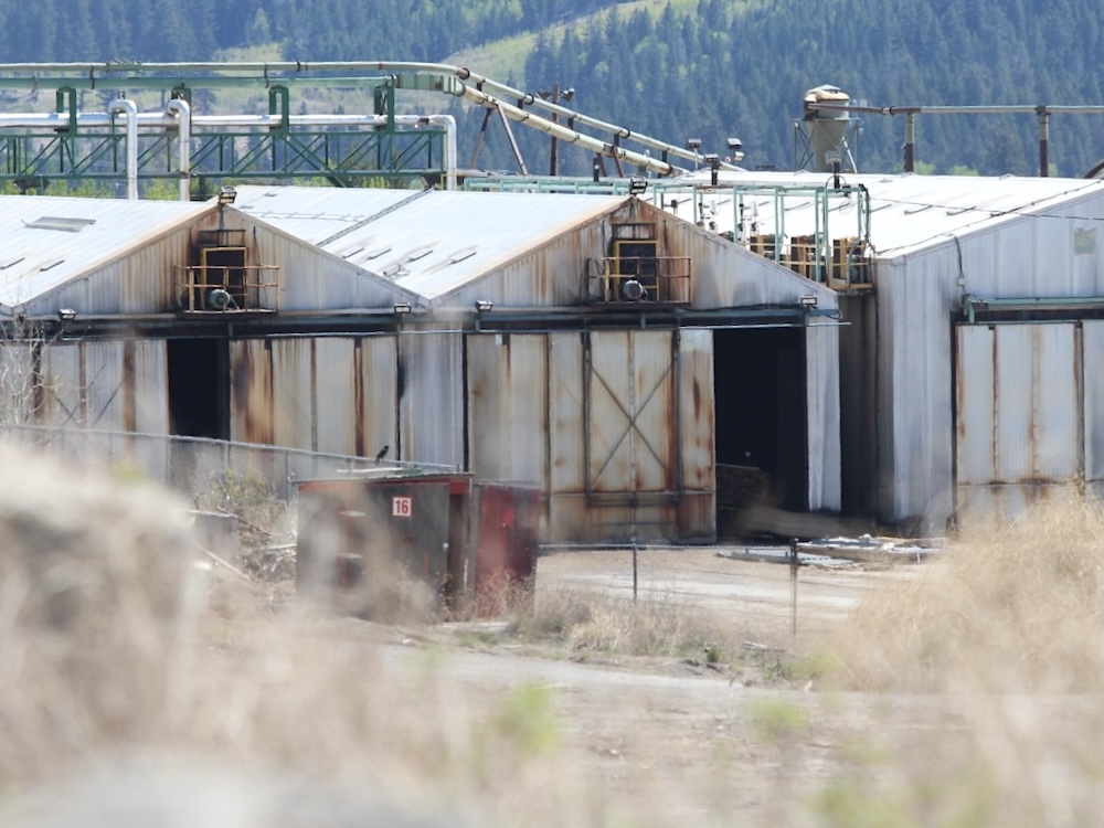 Storage buildings at a mill sit empty and in a state of rusting disrepair.