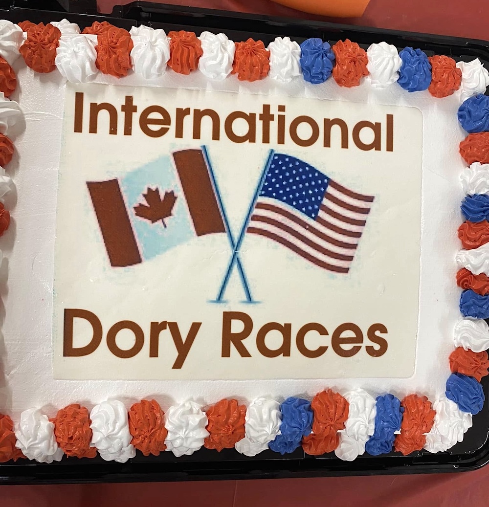 A cake with white icing and the words &lsquo;International Dory Races&rsquo; and the U.S. and Canadian flags.