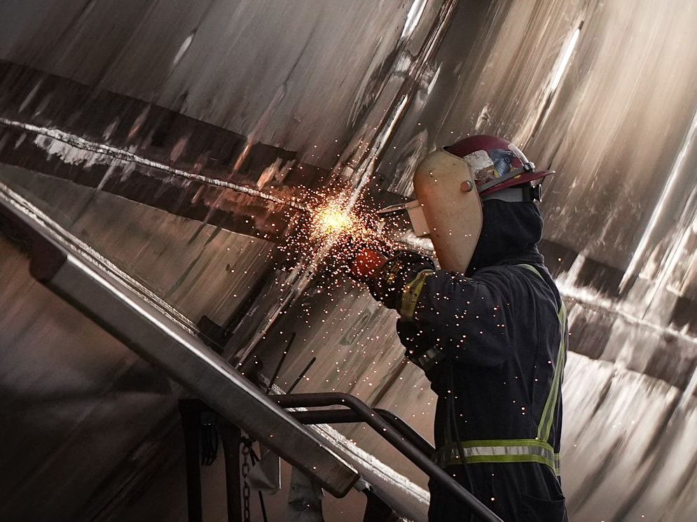 A welder throws sparks against a backdrop of a steel hull.