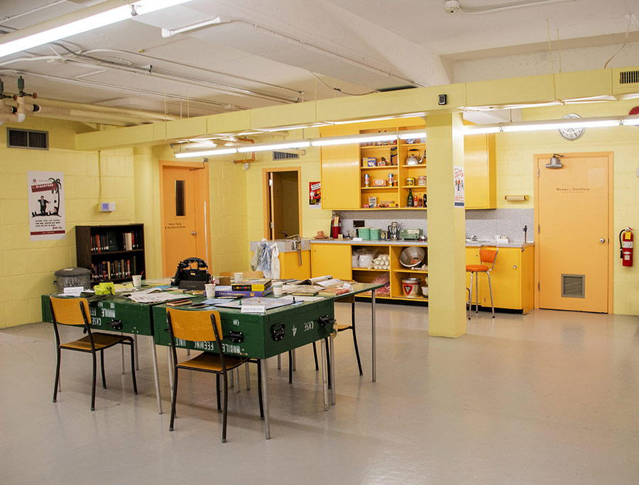 The bunker kitchen has yellow-painted concrete block walls, low ceilings and fluorescent lighting. It features exposed duct work and feels institutional.