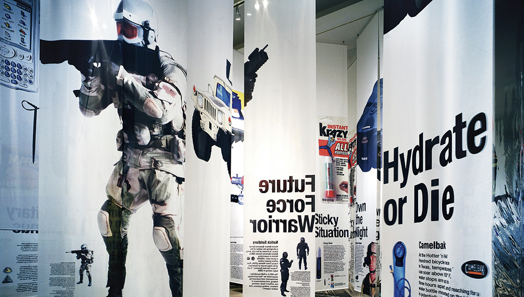 Large vertical banners hang from the ceiling, depicting militaristic images with slogans like “Future Force Warrior” and “Hydrate or Die.”