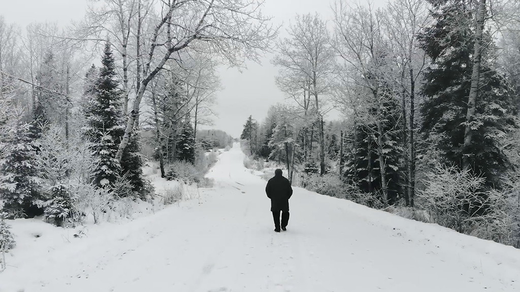 A silhouette of Bruce Mau walks away from the camera in a snow covered landscape.
