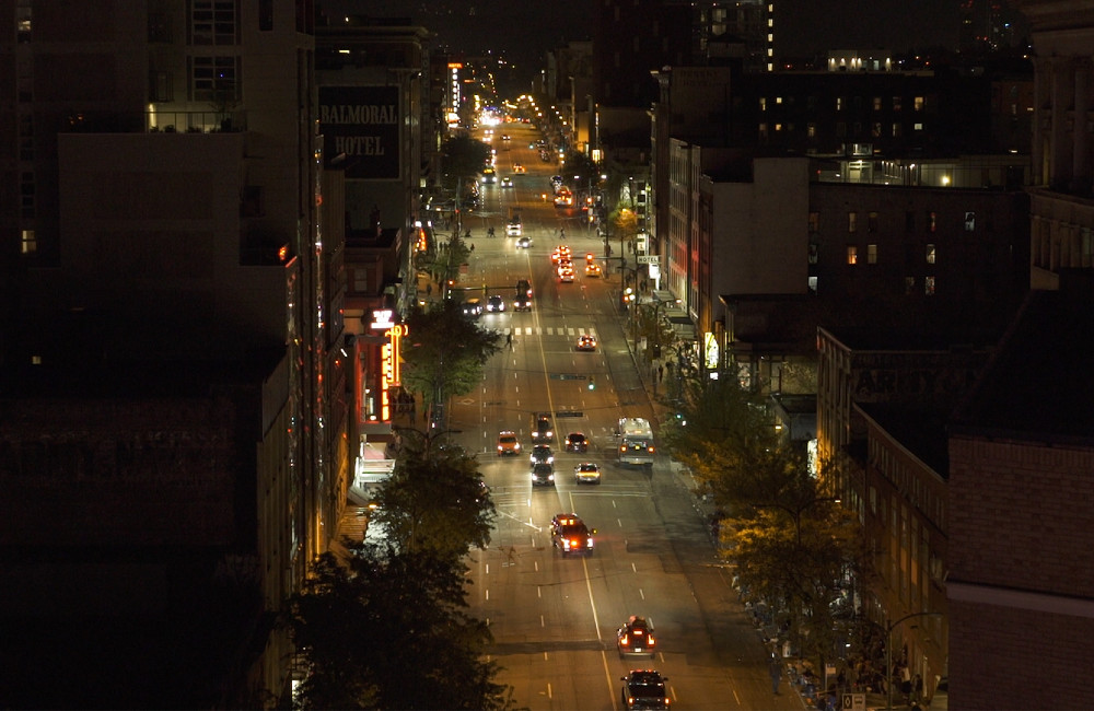 A nighttime photograph depicts light traffic moving up and down East Hastings Street in Vancouver. 
