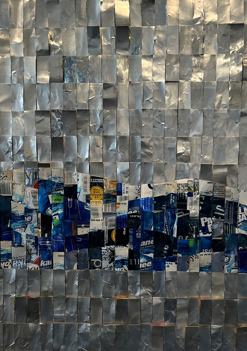 A rather abstract representation of silver water surface and bluish wave, composed of cut and flattened pieces of aluminum cans.