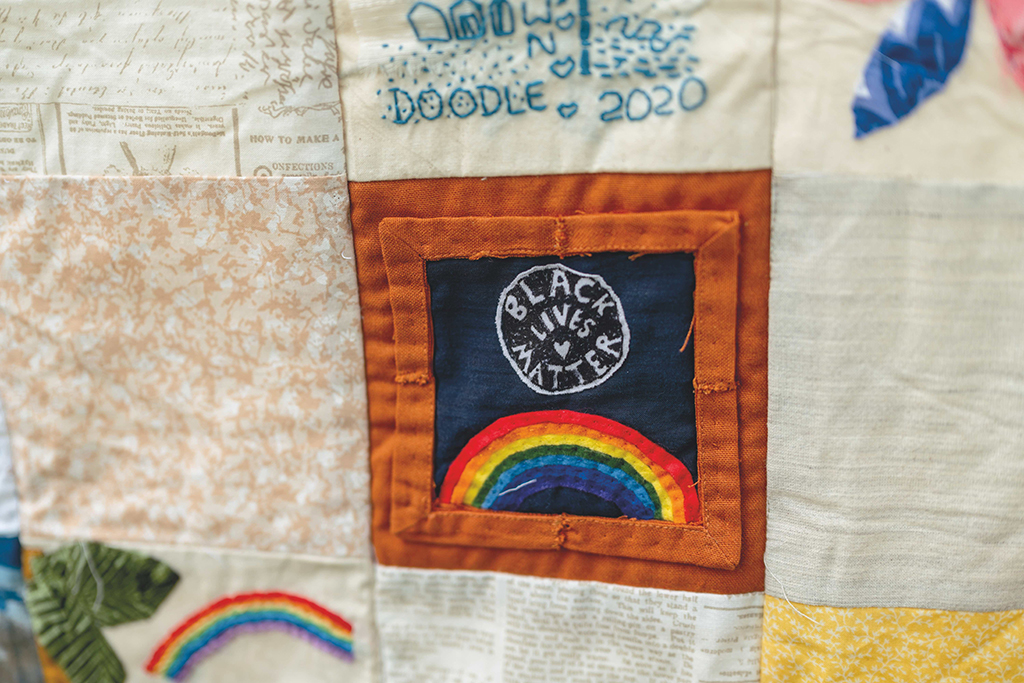 Two stacked images depict two elements of the Quarantine Quilt Project featured in Leanne Prain’s book. The first image is a textile rendition of a laptop computer with a pair of fabric headphones slung over the top left cover of the screen. The second image is a close-up detail of a quilt. One square reads “Black lives matter.”