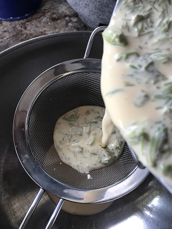 A top-down view of an ice cream base with spruce tips poured through a strainer.