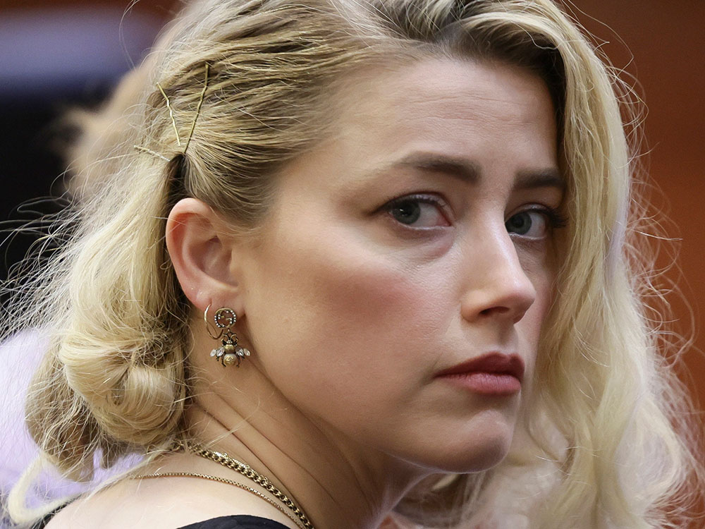Actor Amber Heard looks nervously to the side of the frame. She has blonde hair and is dressed in black.