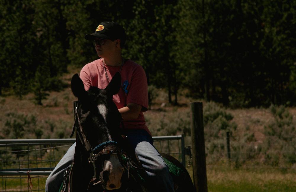 Brianna Stelkia sits on her horse. She is wearing a pink T-shirt and a bass pro shop baseball cap. A silver medal hangs around her neck. 
