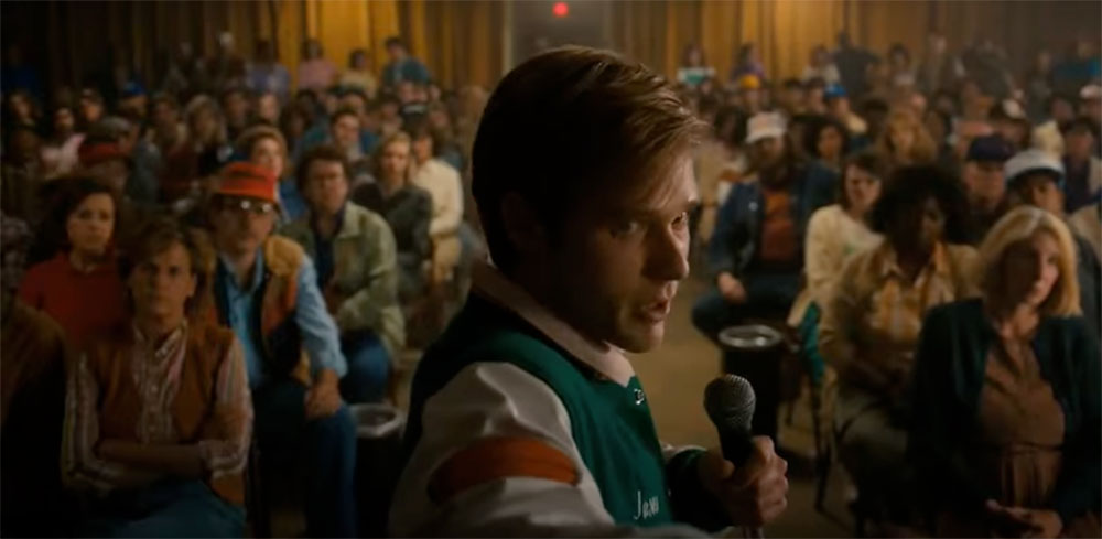 A young man holds a microphone in a gymnasium full of people.