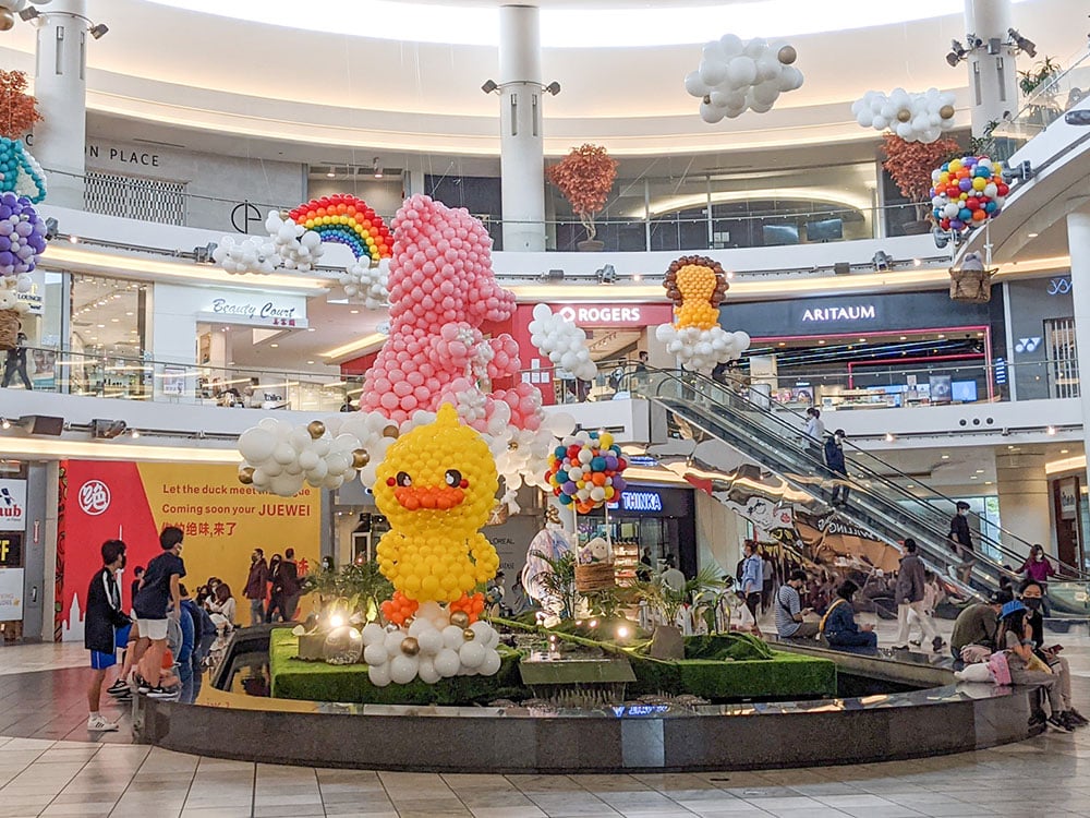 A bunch of yellow and orange balloons in the shape of a yellow duck is the centrepiece of a springtime balloon animal display in an indoor atrium at Aberdeen Centre, a shopping mall in Richmond, BC.