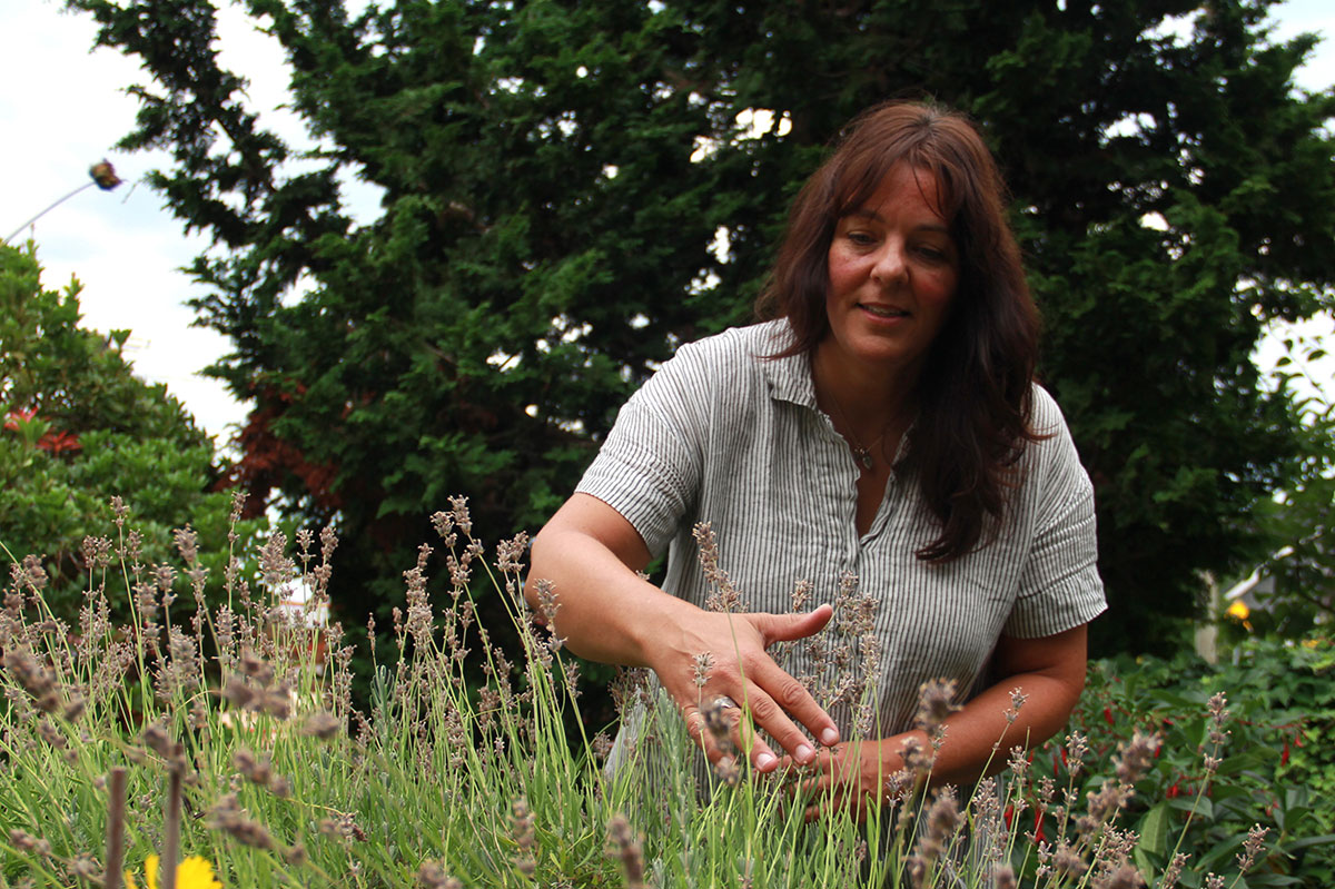 Geneviève Blanchet, a woman with long brown hair wearing a white and grey striped shirt, picks flowers.