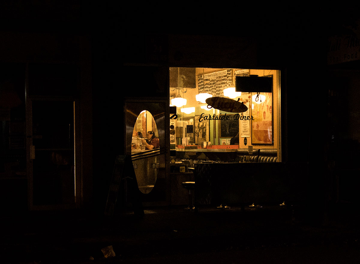 The lights of a diner shine through the window onto a dark street. 