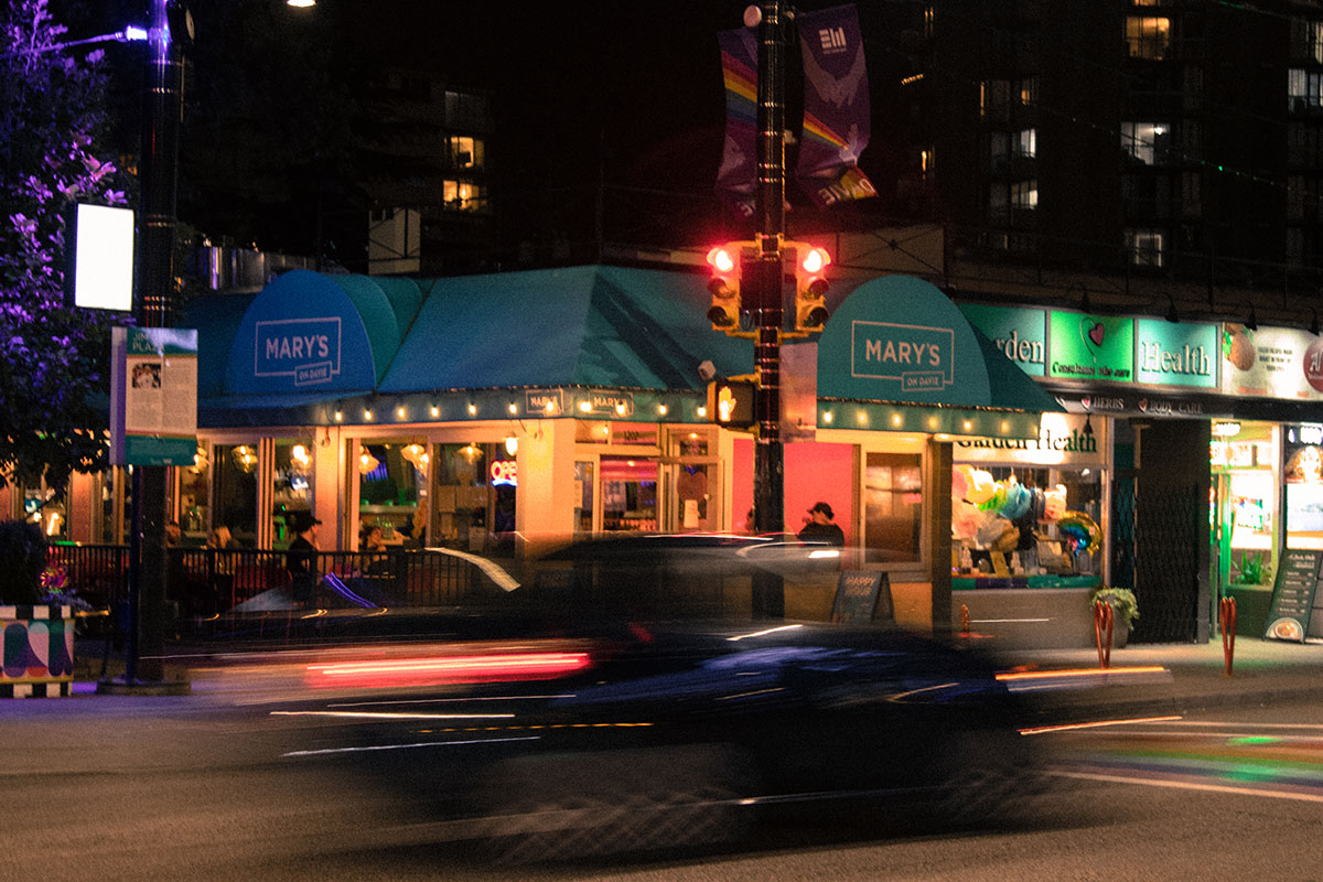 The pastel blue and pink Mary’s on Davie Diner stands in the background as an out of focus black car crosses the rainbow crosswalk in front.