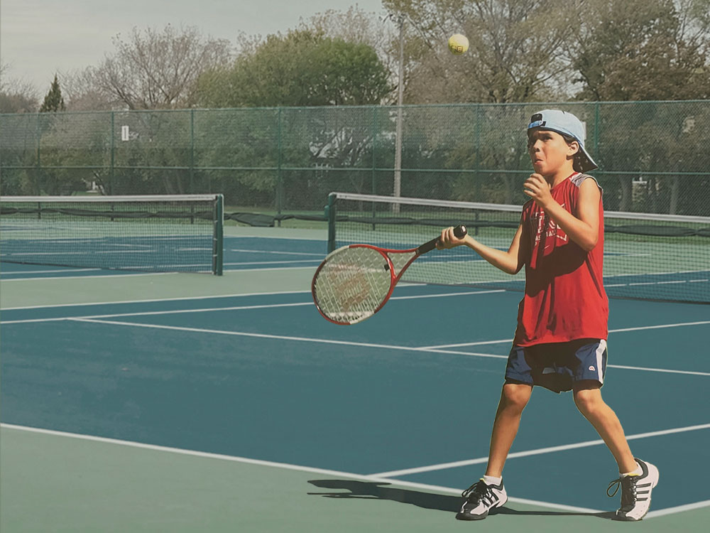 A photo collage depicts Josh Kozelj as a child playing tennis. He is wearing a backwards ball cap, a red sleeveless T-shirt, blue shorts and white sneakers. A tennis ball is in the air above his head and he is moving to hit it with his racket.
