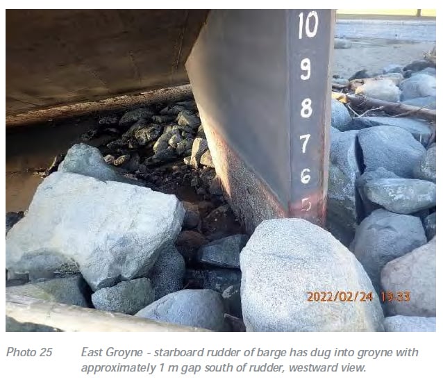 A somewhat grainy photo date-stamped 2022/02/24 shows a barge rudder deeply embedded in a rocky beach.