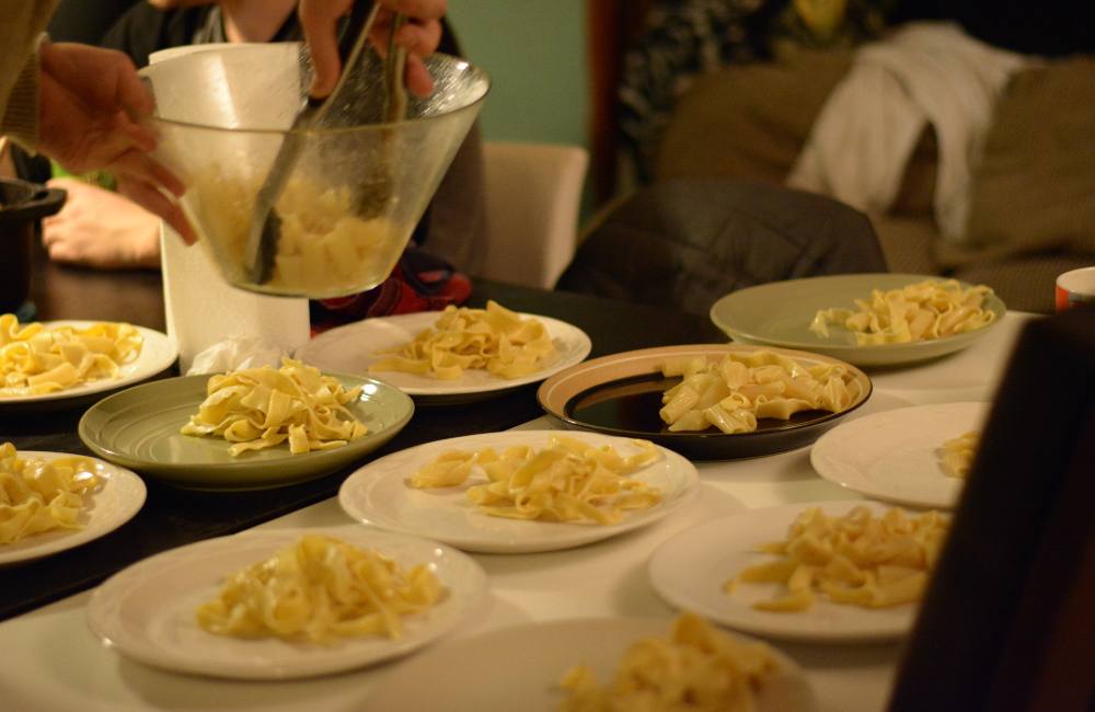 In the top photo, two people are hanging up fresh noodles draped over clothes hangers. In the bottom photo, the freshly cooked noodles have been spun into nests on plates.