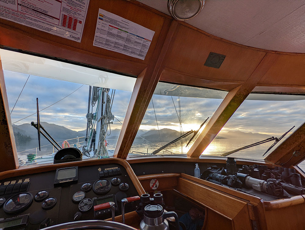 A photo shows the interior of a boat from the perspective of the cockpit. Lots of instrumentation is visible. There are binoculars and camera lenses. The ocean is visible through the cockpit windows.