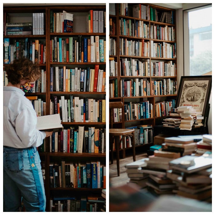 Two vertical photographs of the interior of Reasons to Live bookstore depict, from left, a woman with short curly red hair, a light denim button-down shirt and blue jeans standing and reading a book in front of a mahogany bookshelf that occupies the wall in front of her. Her back is turned to the camera. On the right, a wooden chair stands against a tall wooden bookshelf. Behind it is another wooden chair stacked with books. Diffused light pours in through the window. 