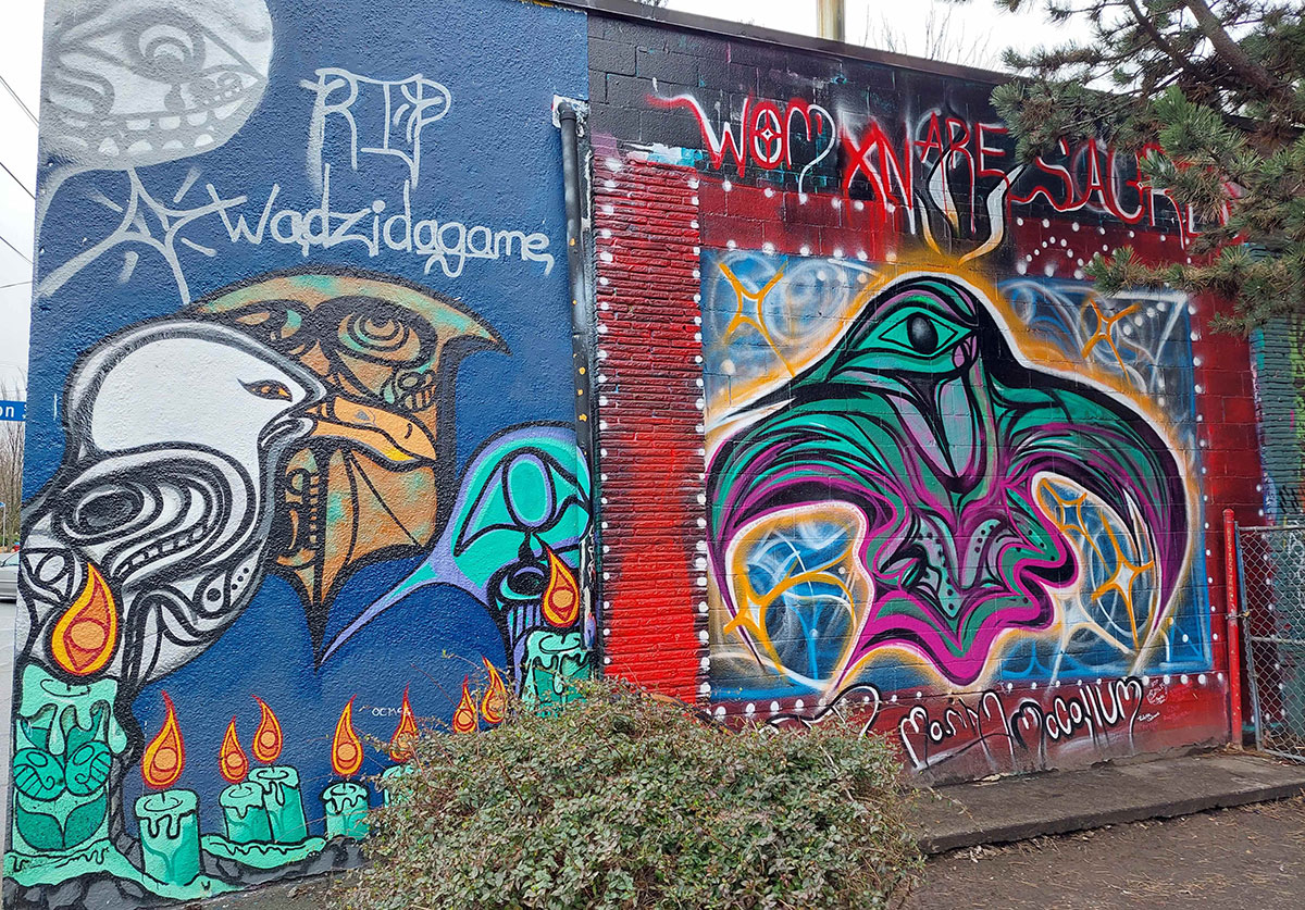 A “Womxn are sacred” mural stands to the right of a blue mural with silver stylized script that reads “RIP Wadzidagame;” stylized turquoise memorial candles line the bottom of the mural.