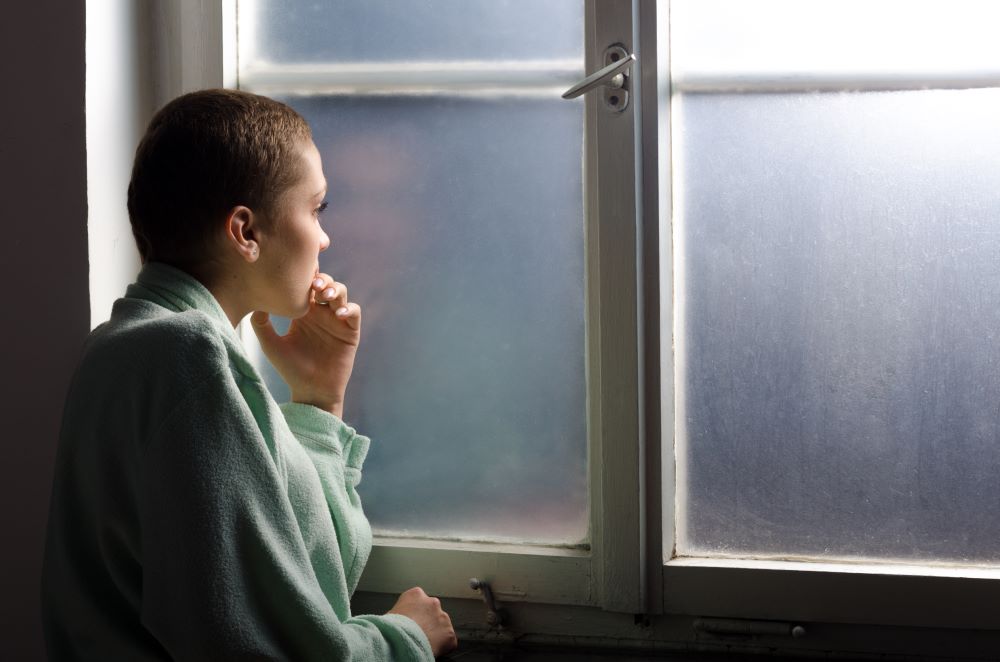 A person in a mint green sweater gazes out a foggy window.