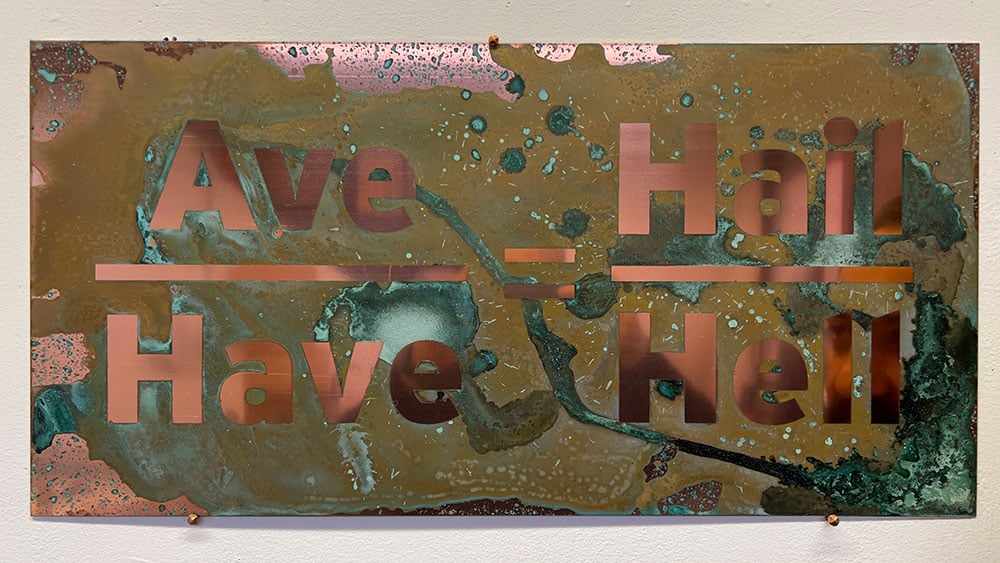 The words “Ave” over “Have” on the left, “Hail” over “Hell” on the right are in bronze san serif text laid over a polished copper plate oxidized with urine.