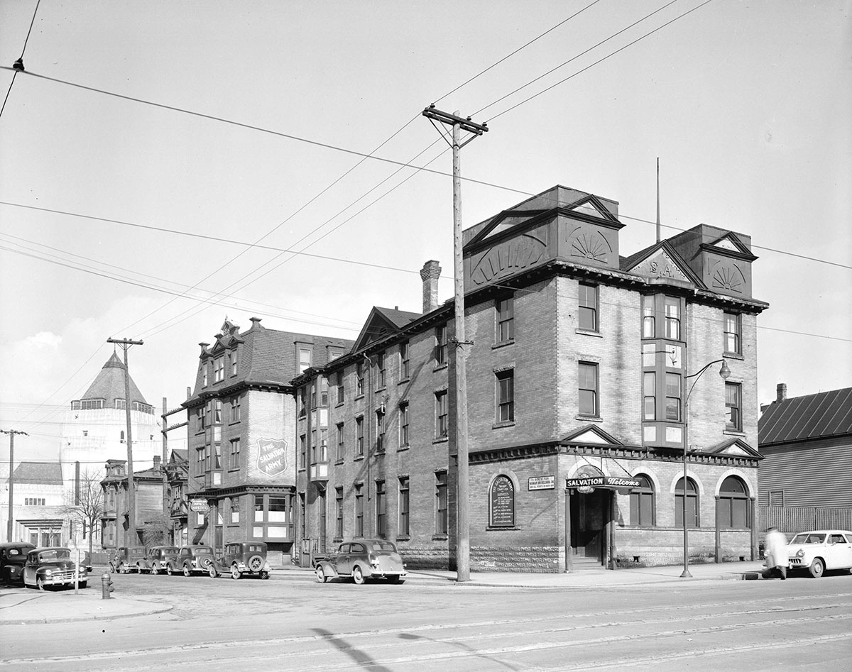 A black and white photo shows a brick building with the Salvation Army crest painted on the side.