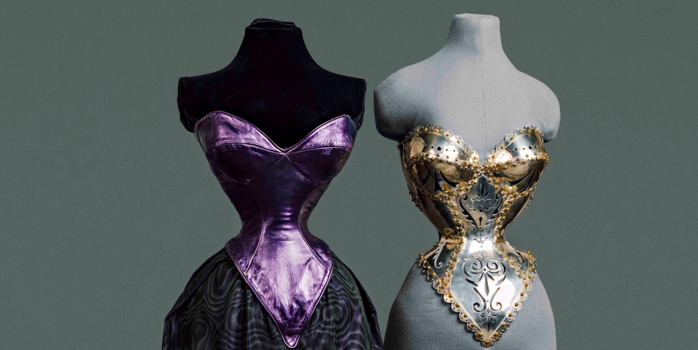 Two sparkling corsets are on side-by-side mannequins, a black mannequin on the left and a grey mannequin on the right. The corset on the left is a metallic purple, attached to a ballgown skirt. The corset on the right is silver and studded with gold. 
