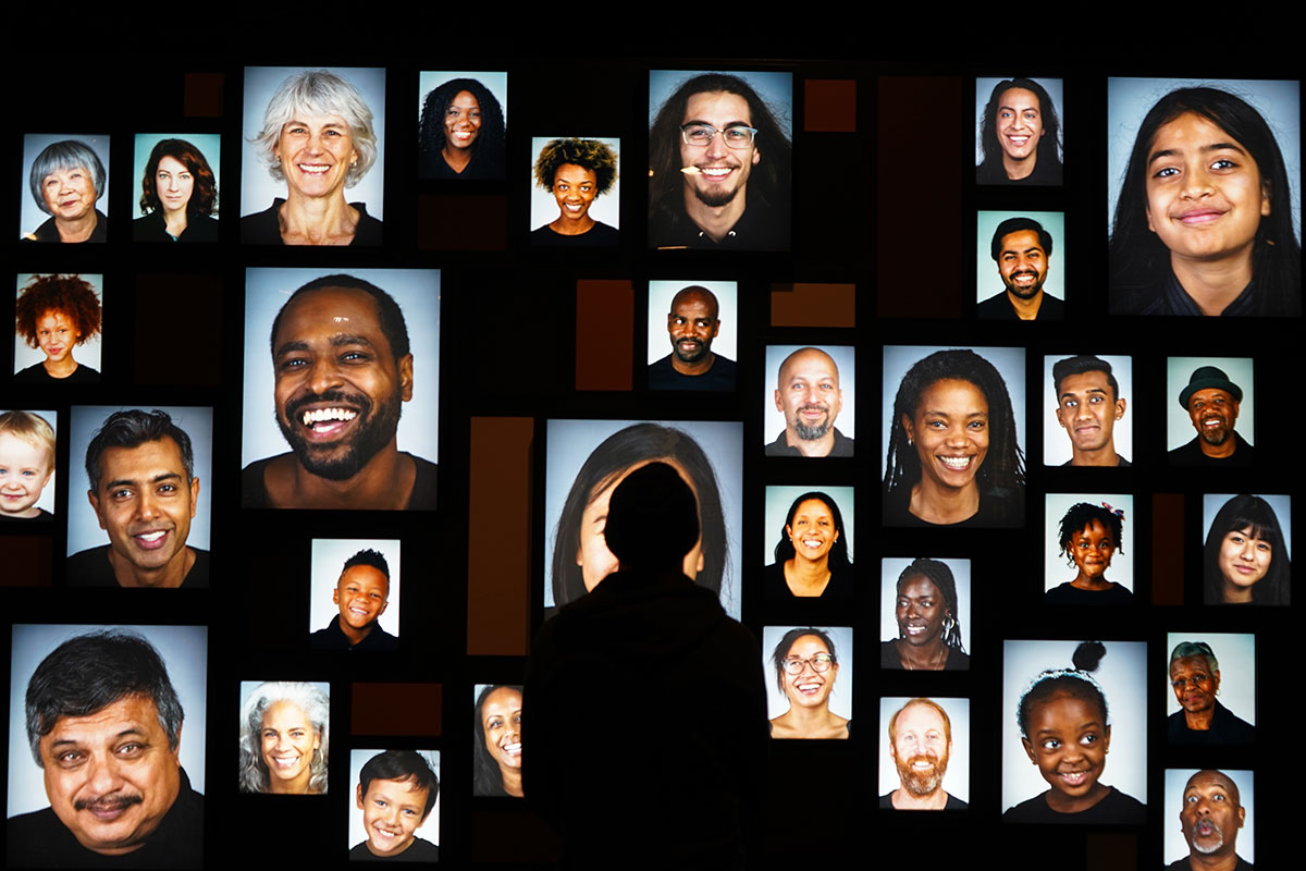 A projection of photographs of human faces on a black screen.