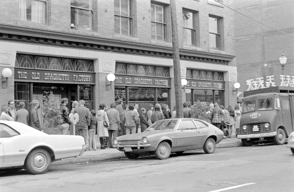 A black and white photo shows people lined up outside the Old Spaghetti Factory.
