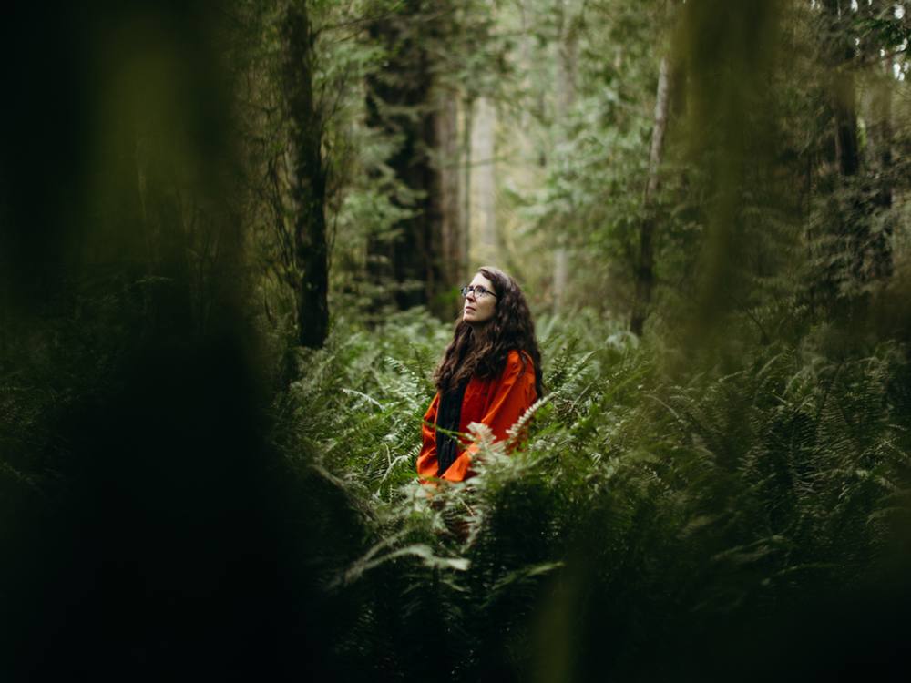 Amanda Lewis sits in a stand of tall evergreens, surrounded by ferns.