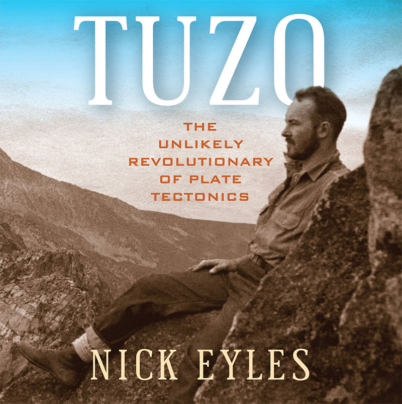 The book cover image for Tuzo: The Unlikely Revolutionary of Plate Tectonics features an archival sepia photo of Canadian geologist John Wilson Tuzo seated on a rocky outdoor landscape against a bright blue sky.