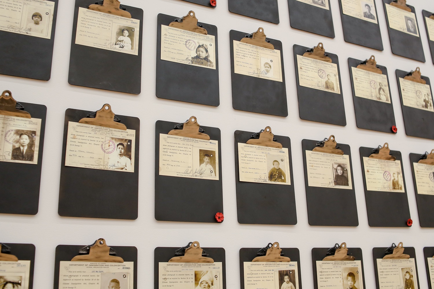 A wall of old IDs on clipboards that show pictures of ethnically Chinese children on identification cards.