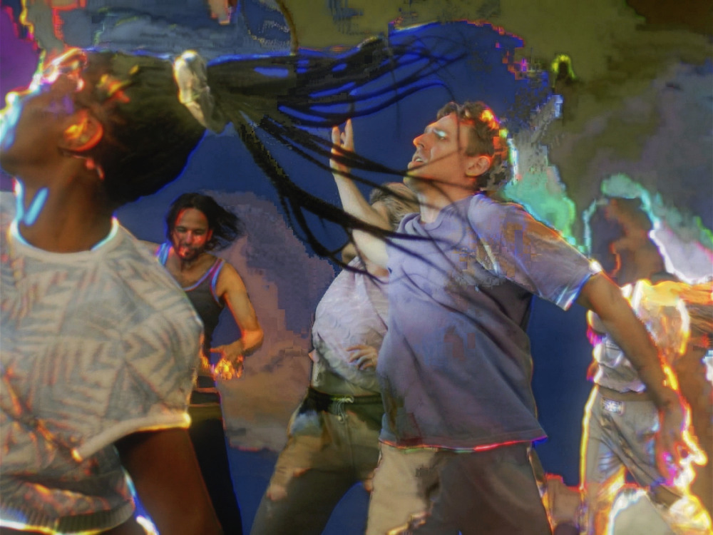 A digital video still shows colours and light patterns melding into each other as a group of people in contemporary street clothes move their bodies in dance. They are facing the left of the frame.