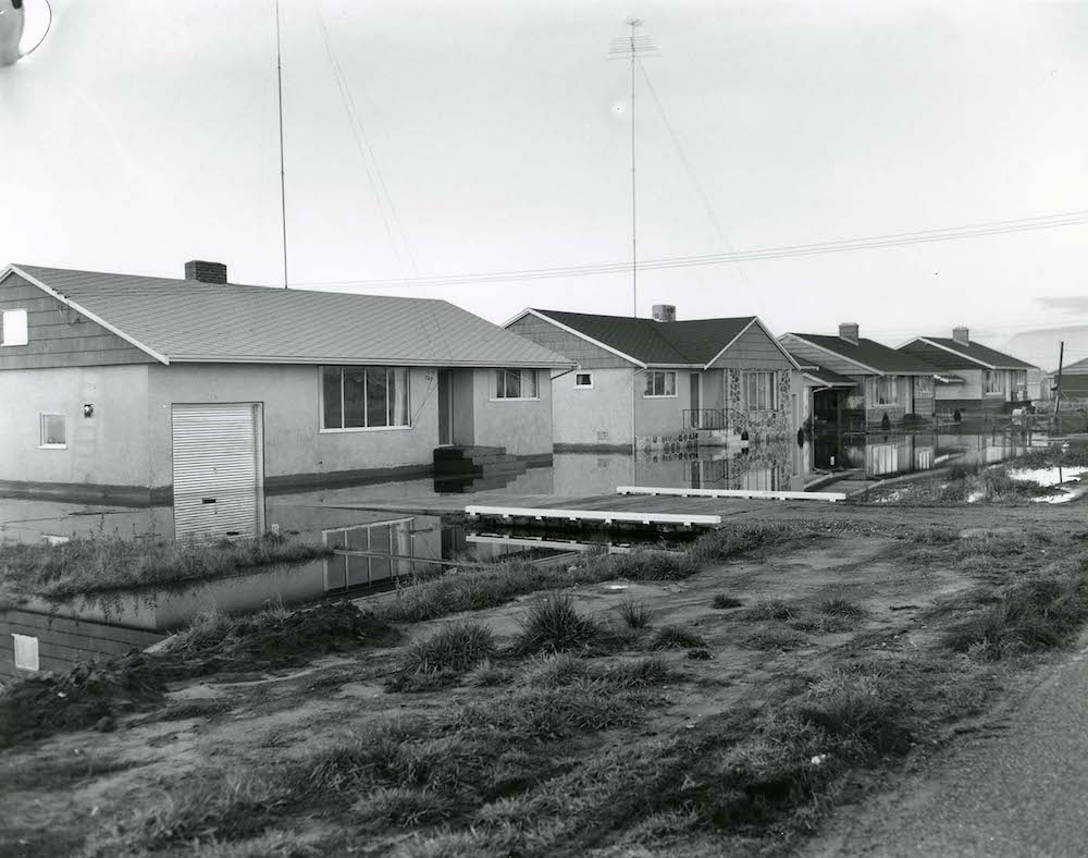 A black-and-white photo of houses with waterlogged yards.
