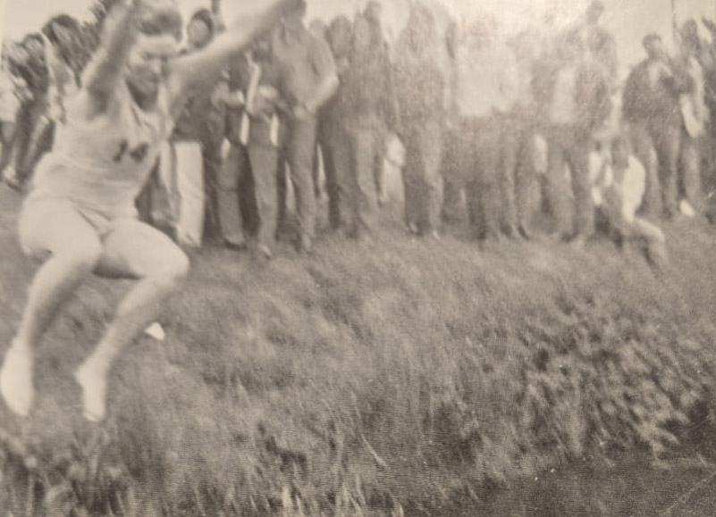 A teenage boy leaps over a ditch as a crowd watches.