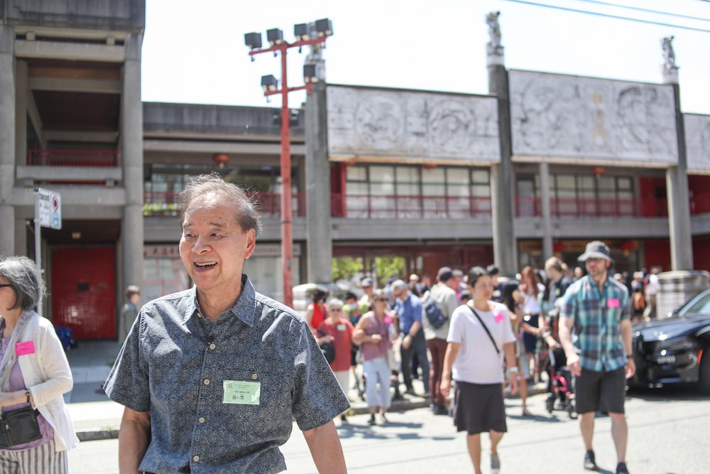 一名身穿短袖紐扣上衣的華裔男子穿過溫哥華唐人街的街道，身後有一群人。