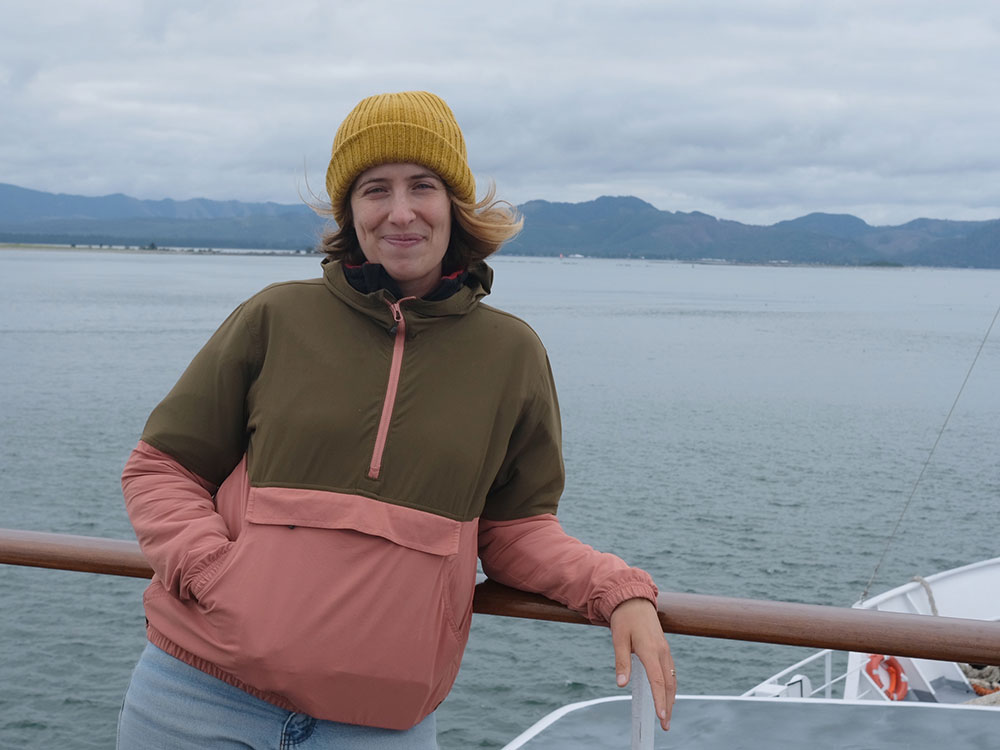 Author Laura Trethewey is on a boat, with the ocean visible in the background. Her hair is swept back by the wind. She wears a yellow toque.