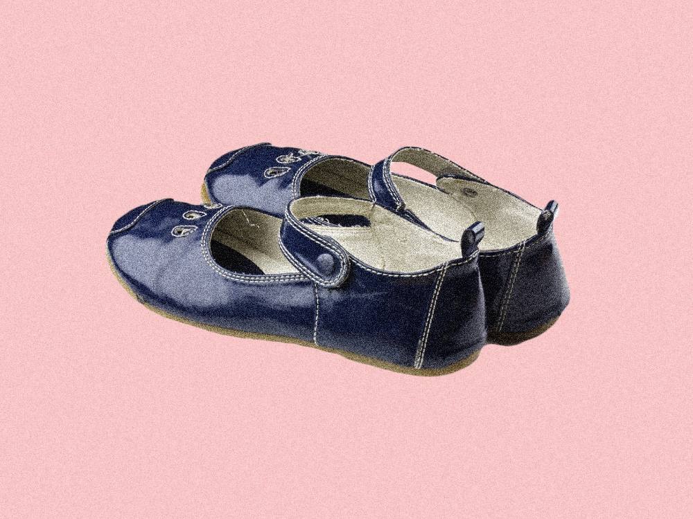 A pair of black children's shoes sits superimposed on a bright pink backdrop. 