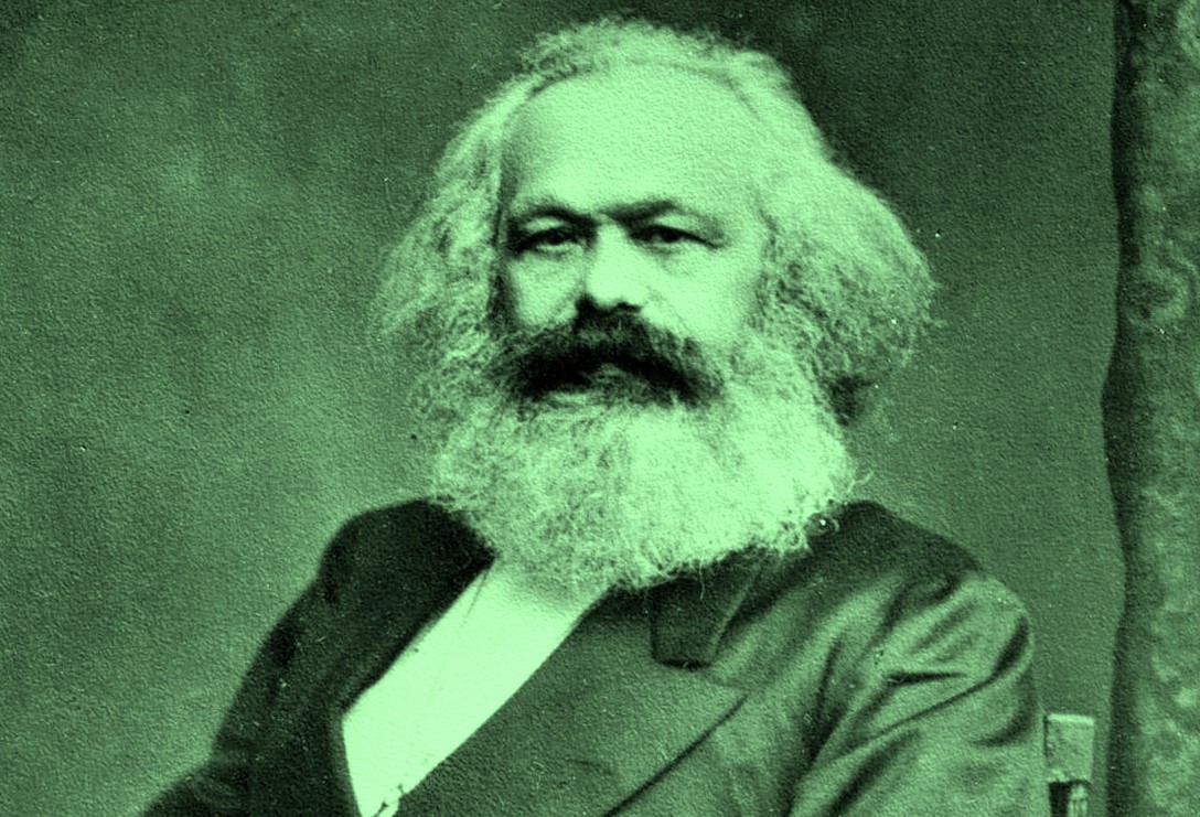 An archival portrait of Karl Marx features a man with white bushy hair and a beard looking directly at the camera. He is seated, wearing a suit jacket over a white shirt. The photograph is tinted green.