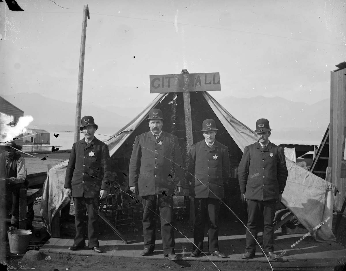 A black and white photo shows four men standing in front of a canvas tent.