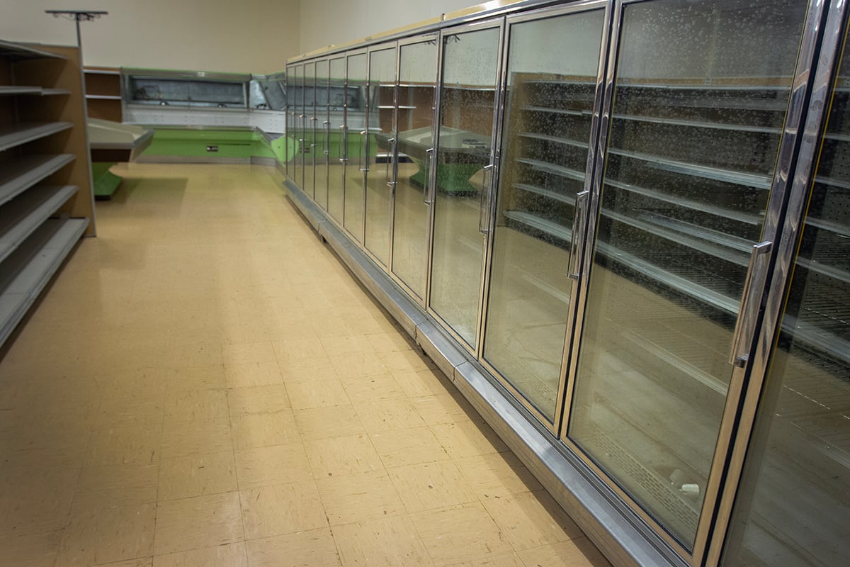 The freezer aisle in an empty grocery store shows a row of glass doors.