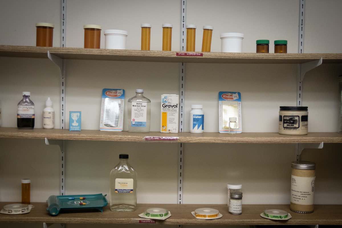 Three shelves hold medical supplies that appear to be very dated, including witch hazel, Gravol and pill bottles.