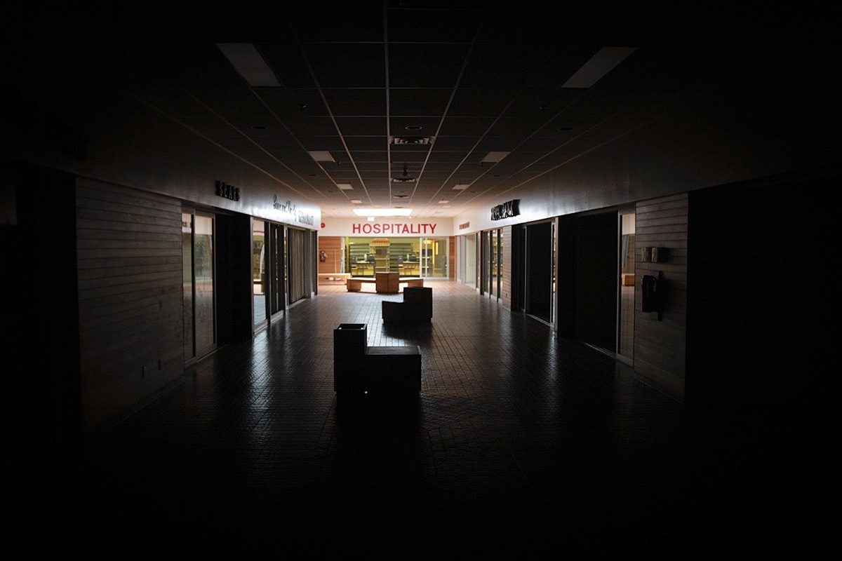 A sign over an empty store at the end of a darkened corridor says “hospitality” in all caps.