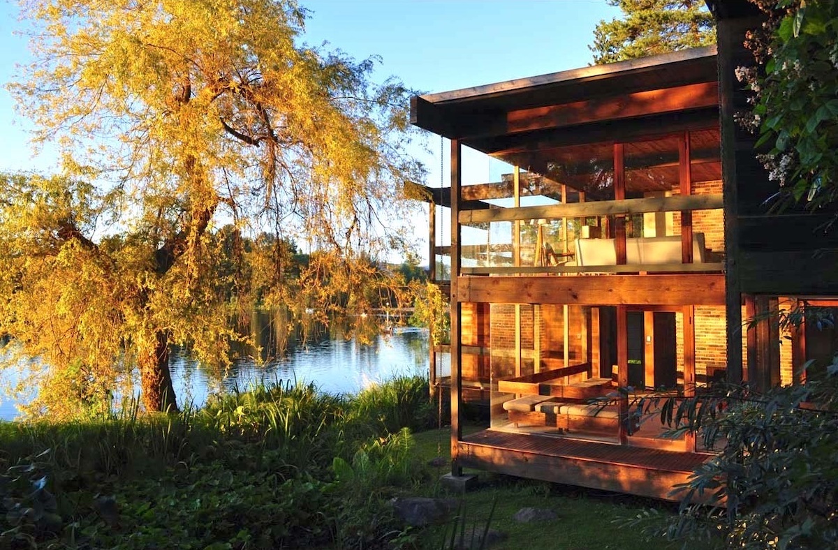 A glass house on a lake on a sunny day from the side.