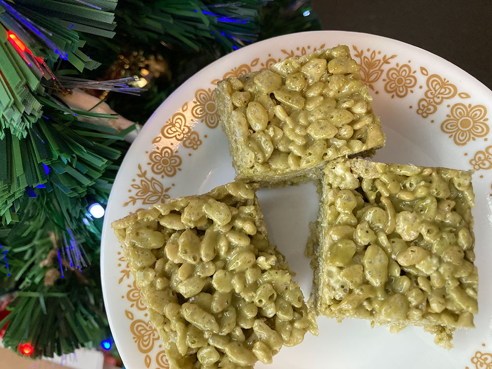 An overhead shot of matcha Rice Krispies squares on a vintage plate, near a Christmas tree.