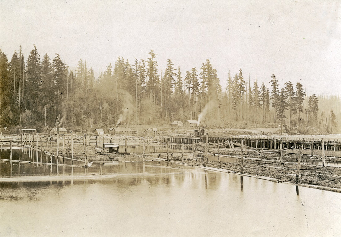 A sepia-toned photo shows log booms in the water, flanked by a wooden bridge with a steam donkey that is spewing steam. Some buildings are visible on the shore.