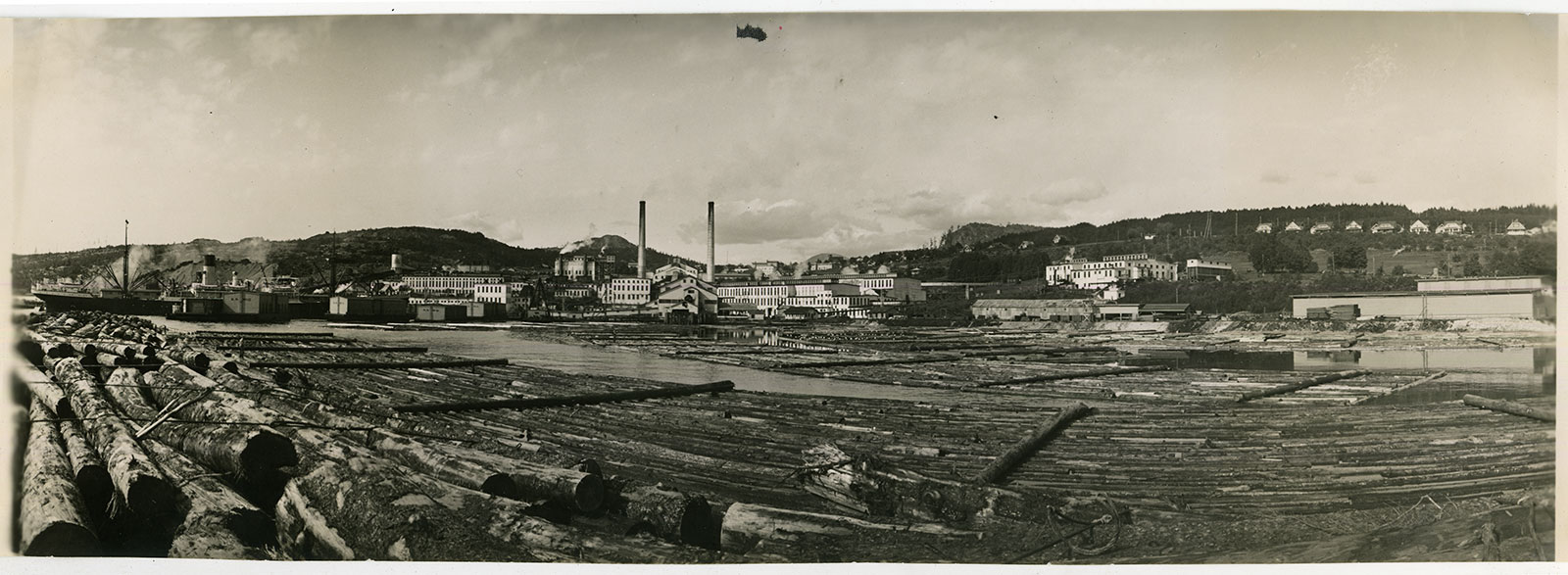 Log booms in the water in the foreground; in the background, the newsprint mill and Townsite.
